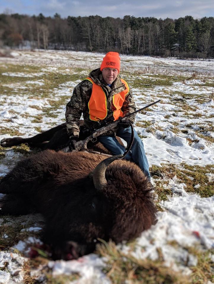 Hunter holding rifle next to bison kill