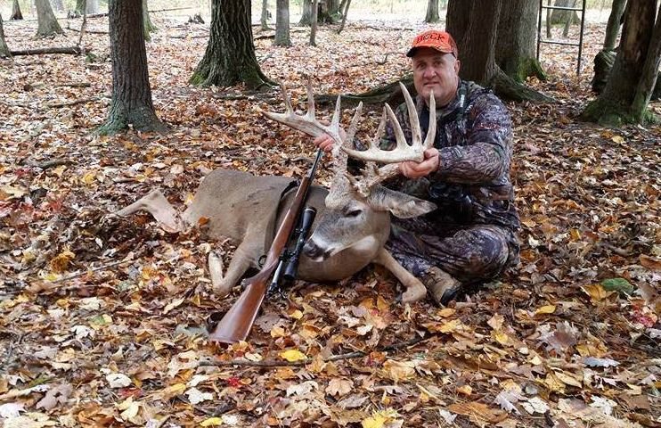 A hunter on a bed of leaves posing with a whitetail deer