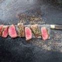 Aged venison cut with butcher knife and salted with rub on a wooden cutting board