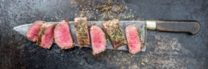 Aged venison cut with butcher knife and salted with rub on a wooden cutting board